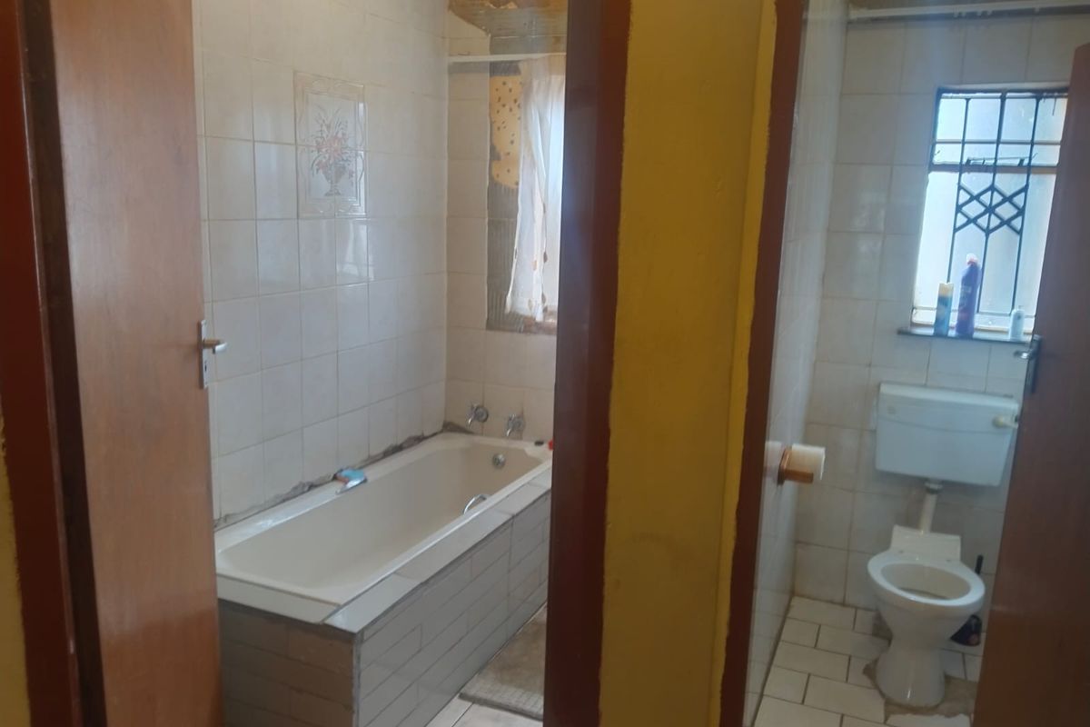A dated bathroom featuring a built-in bathtub and a separate toilet area with tiled walls and floors.