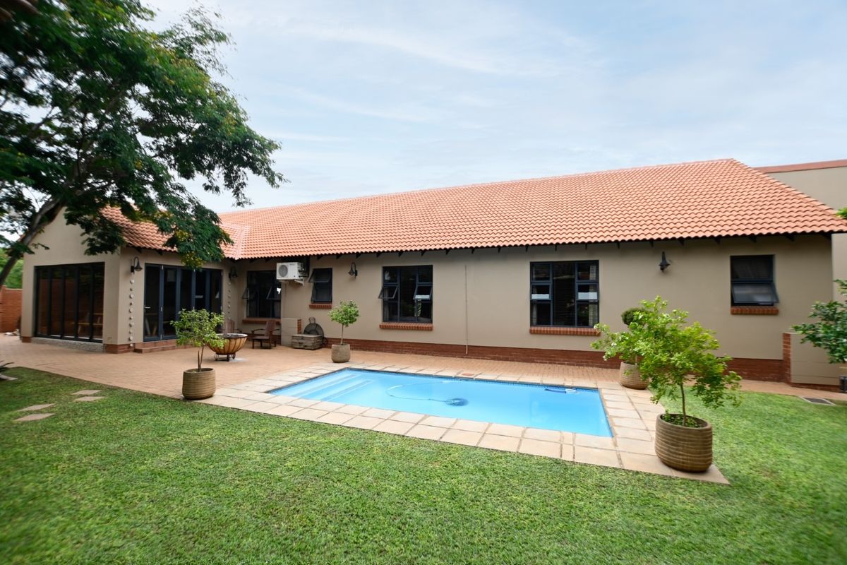 Rear exterior view featuring a swimming pool, paved patio area, and a well-maintained garden with a tiled roof house facade.