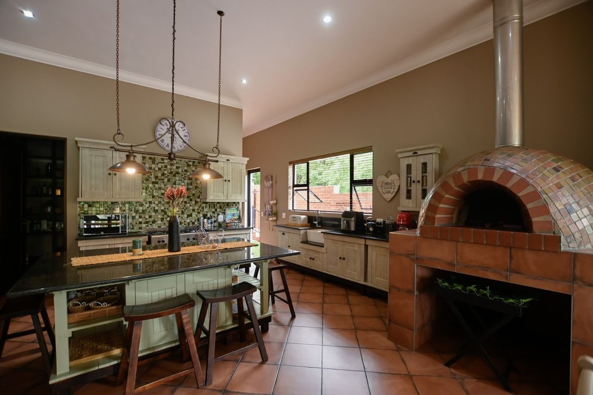 Spacious kitchen featuring a large central island, granite countertops, mosaic tile backsplash, and a built-in brick pizza oven.