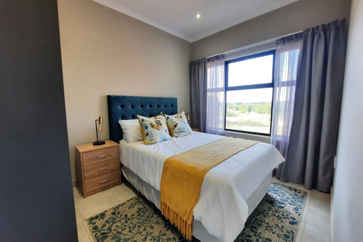 A well-lit bedroom featuring neutral wall tones, tiled flooring, and a large window providing natural light and scenic views.