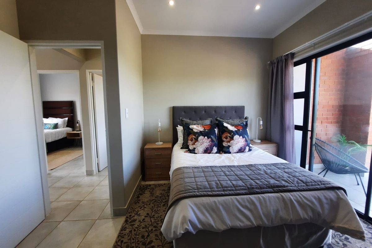 A well-lit bedroom featuring tiled flooring, recessed ceiling lighting, and large sliding glass doors providing direct access to an outdoor patio area.