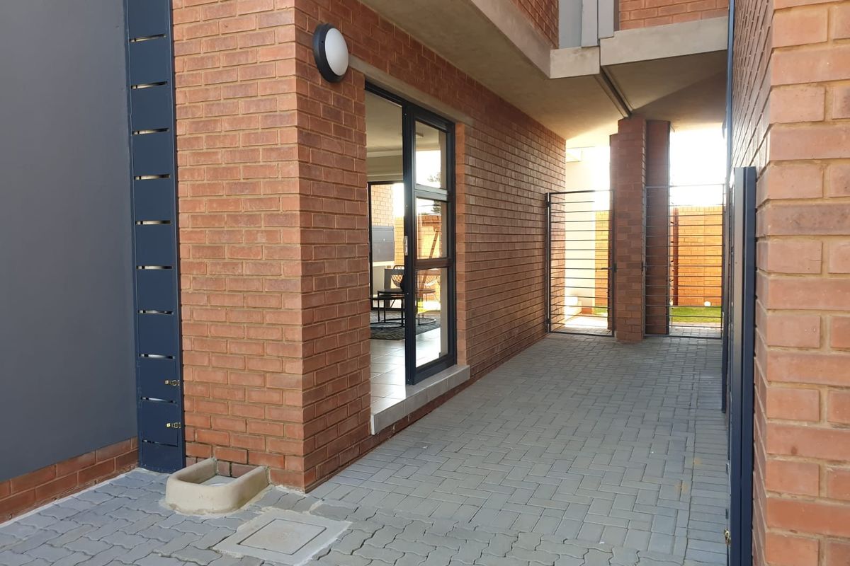 A view of the exterior side passage and entrance area featuring face brick walls, paved flooring, and a modern glass sliding door.