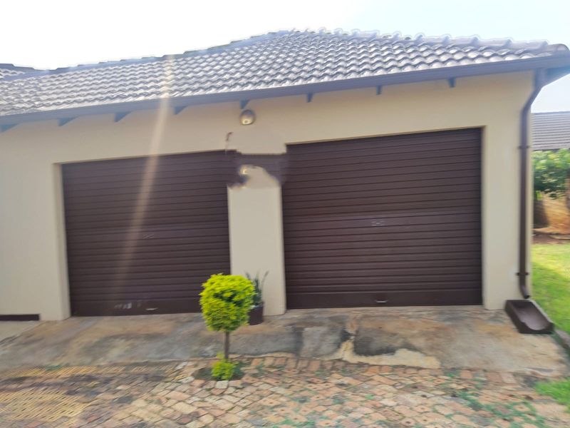 A double garage with brown roller doors, tiled roof, and paved driveway, showing signs of wear on the exterior wall and paving.