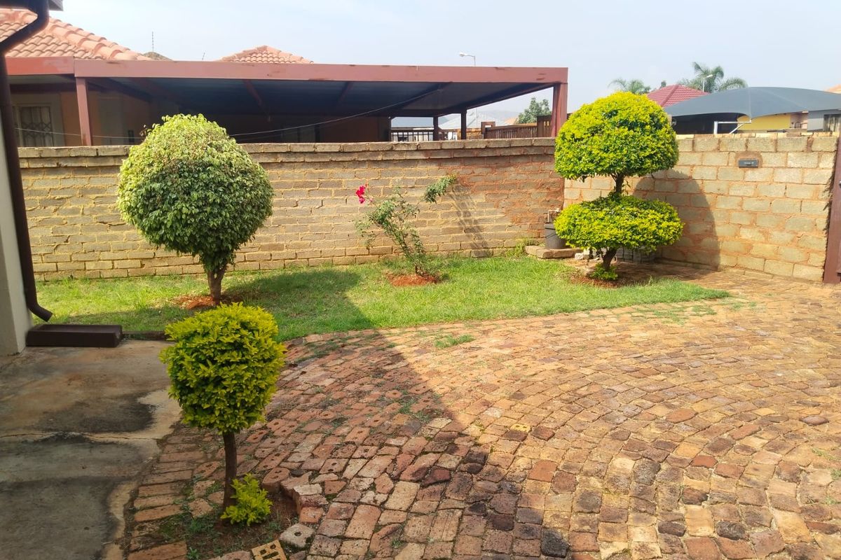 A rear garden area featuring a paved patio, a brick boundary wall, and a covered outdoor structure.