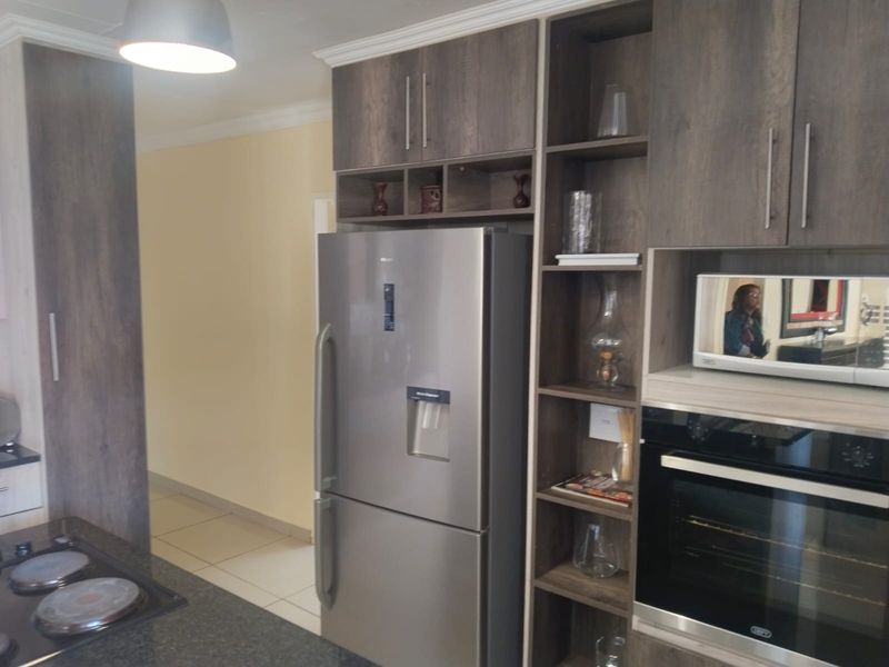 Modern kitchen featuring dark wood-grain cabinetry, integrated oven, built-in microwave, and a stone countertop with a hob.