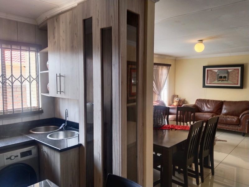 Open plan living area featuring a modern kitchen with granite countertops, double sink, and built-in cabinetry, seamlessly flowing into the dining and lounge space.