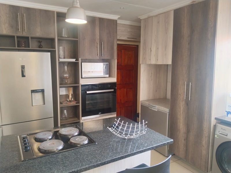 Modern kitchen featuring two-tone cabinetry, granite countertops, a central island with an electric hob, and integrated built-in appliances.
