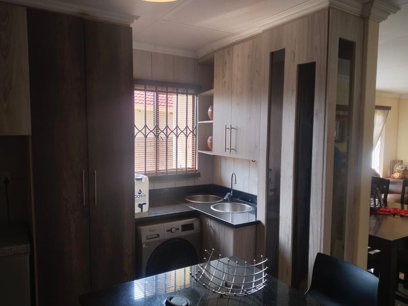 Compact scullery area featuring modern wood-finish cabinetry, granite countertops, double sinks, and dedicated space for laundry appliances.