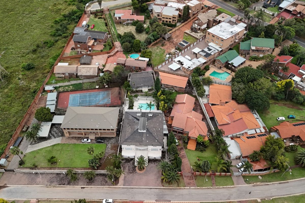 Aerial view of a residential property featuring a swimming pool, tennis court, and multiple buildings within a suburban neighborhood setting.