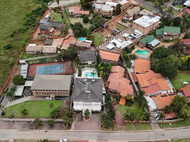 Aerial view of a residential property featuring a swimming pool, tennis court, and multiple buildings within a suburban neighborhood setting.