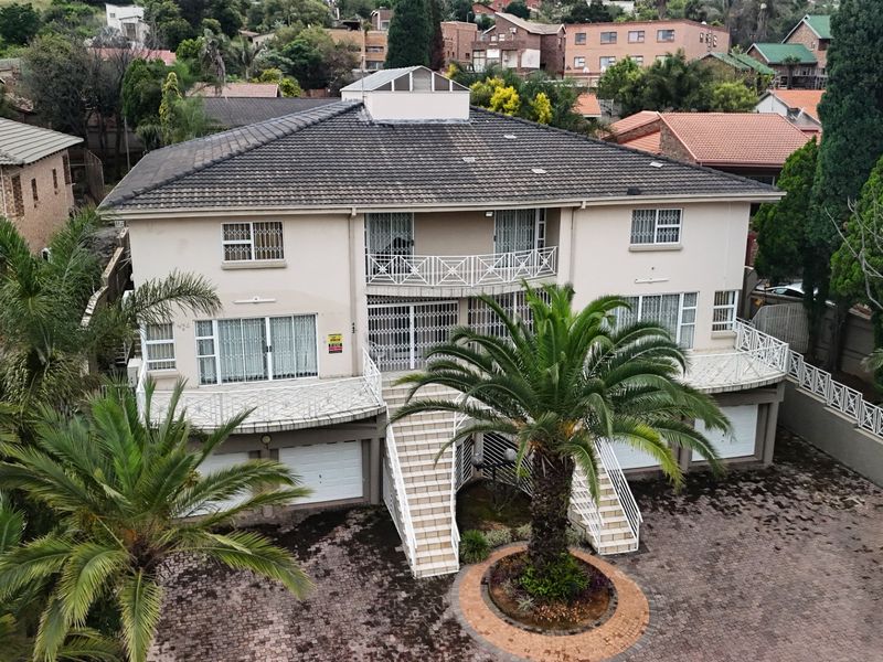 Aerial view of a multi-level residential property featuring a tiled roof, paved driveway, double garage, and elevated balconies with security gates.