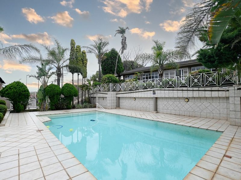 Outdoor swimming pool area featuring a tiled surround, retaining wall with decorative metal fencing, and established garden landscaping.