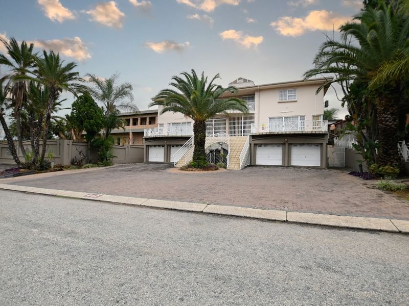 Front elevation of a multi-level house featuring a paved driveway, triple garage, and a raised balcony with external staircase access.
