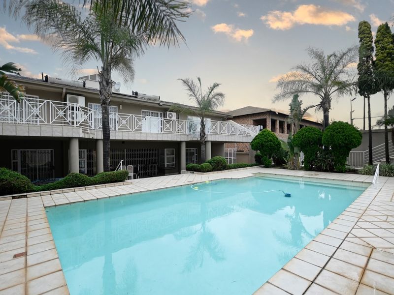 A spacious outdoor pool area featuring a tiled surround, a large swimming pool, and a balcony with metal balustrades overlooking the garden.