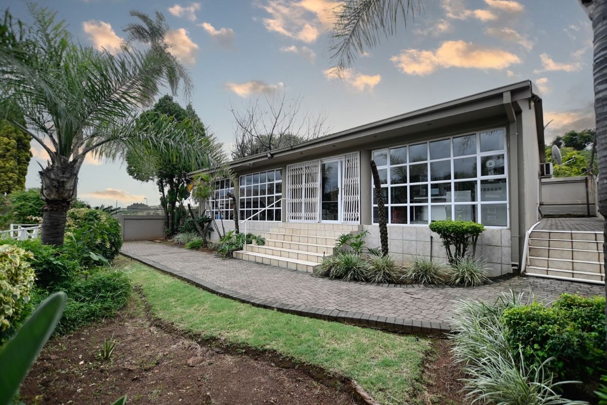 Rear exterior view of the house featuring a paved walkway, tiled entrance stairs, and large grid-pattern windows with security gates.