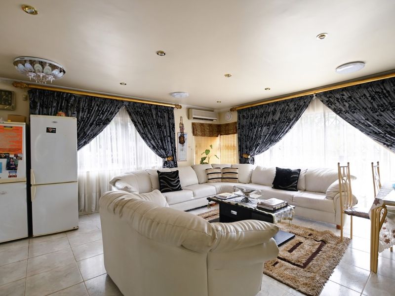 A spacious living area featuring tiled flooring, recessed ceiling lighting, and a wall-mounted air conditioning unit, providing a functional and comfortable living space.
