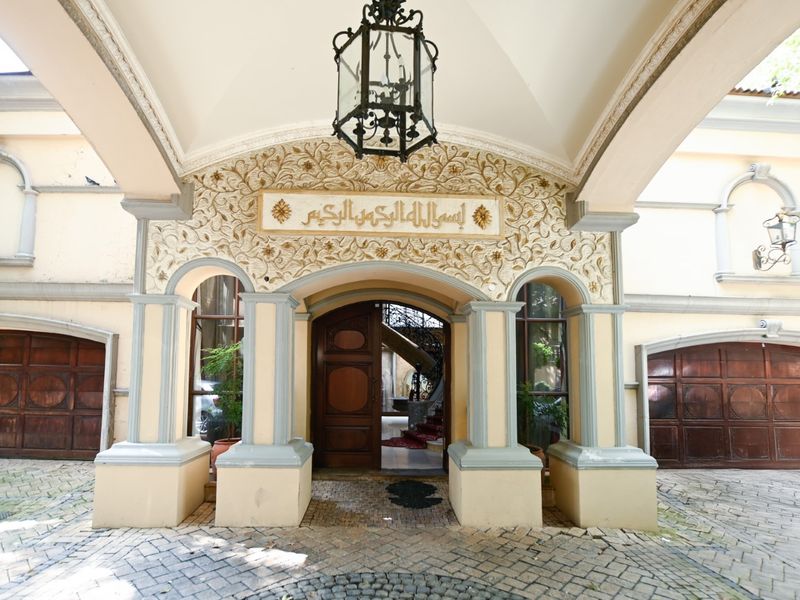 Grand entrance featuring ornate stone detailing, arched doorways, and a covered portico with a classic lantern fixture and cobblestone driveway.