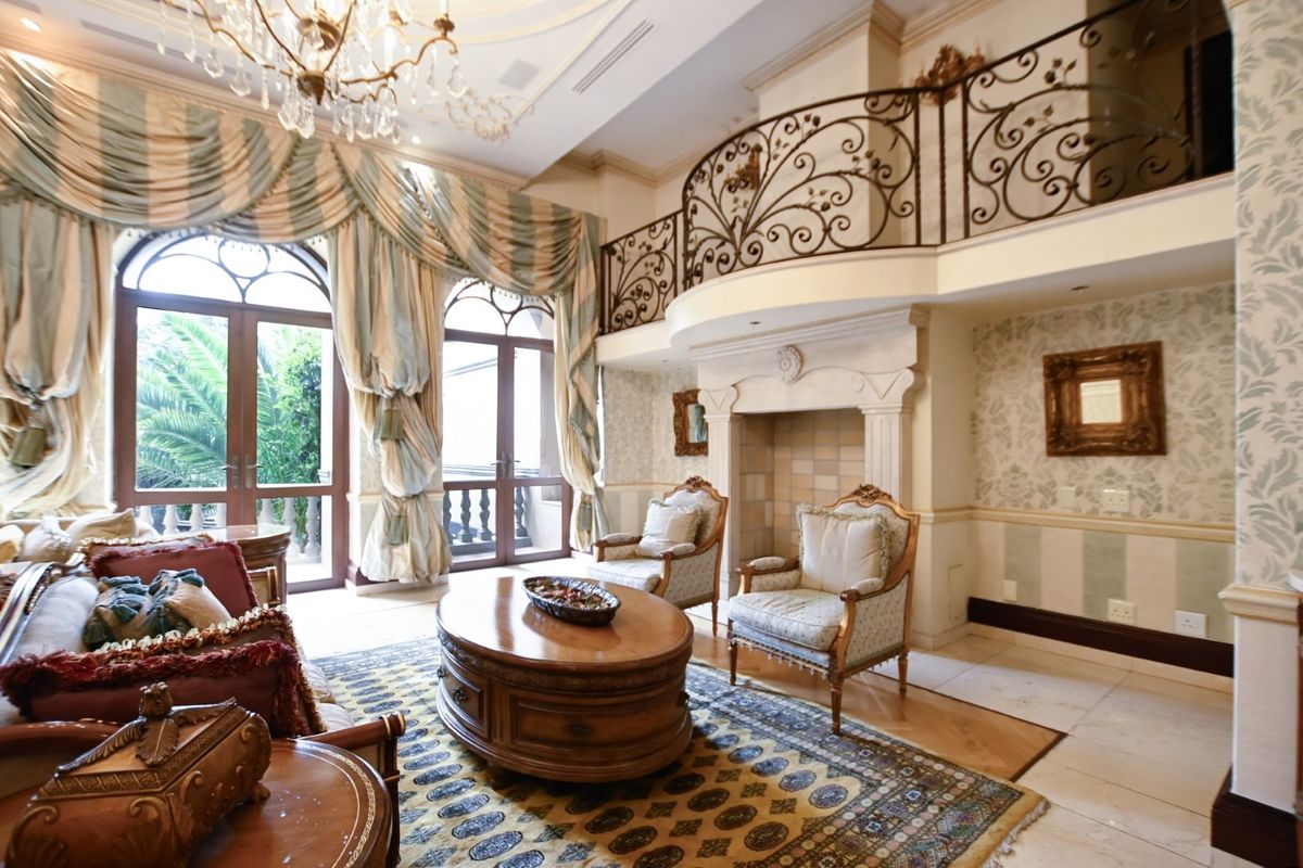 Elegant double-volume living room featuring a stone fireplace, ornate wrought iron mezzanine railing, and arched french doors leading to an outdoor area.