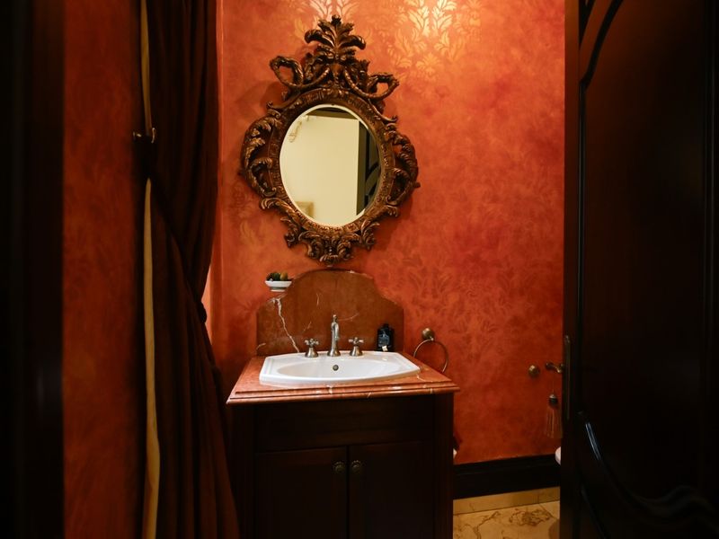 A powder room featuring a marble-topped vanity cabinet, decorative wall finishes, and a classic ornate mirror.