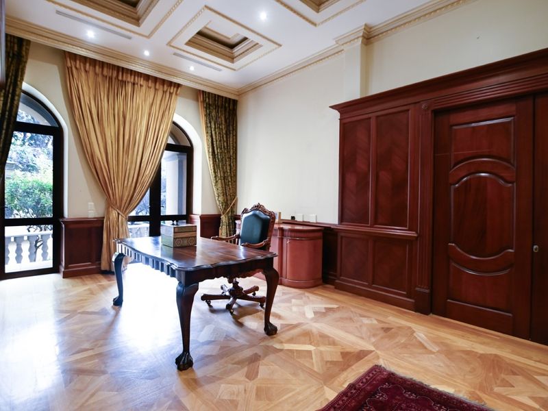 Elegant home office featuring rich wood paneling, intricate parquet flooring, a coffered ceiling with recessed lighting, and arched windows providing natural light.