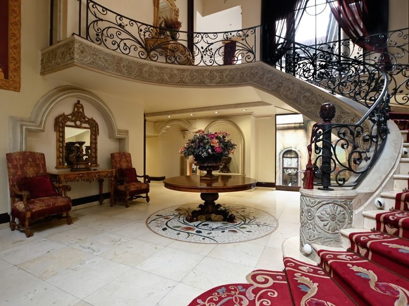 Grand entrance foyer featuring a sweeping stone staircase with ornate wrought iron railings, marble flooring with decorative mosaic inlay, and elegant arched wall niches.