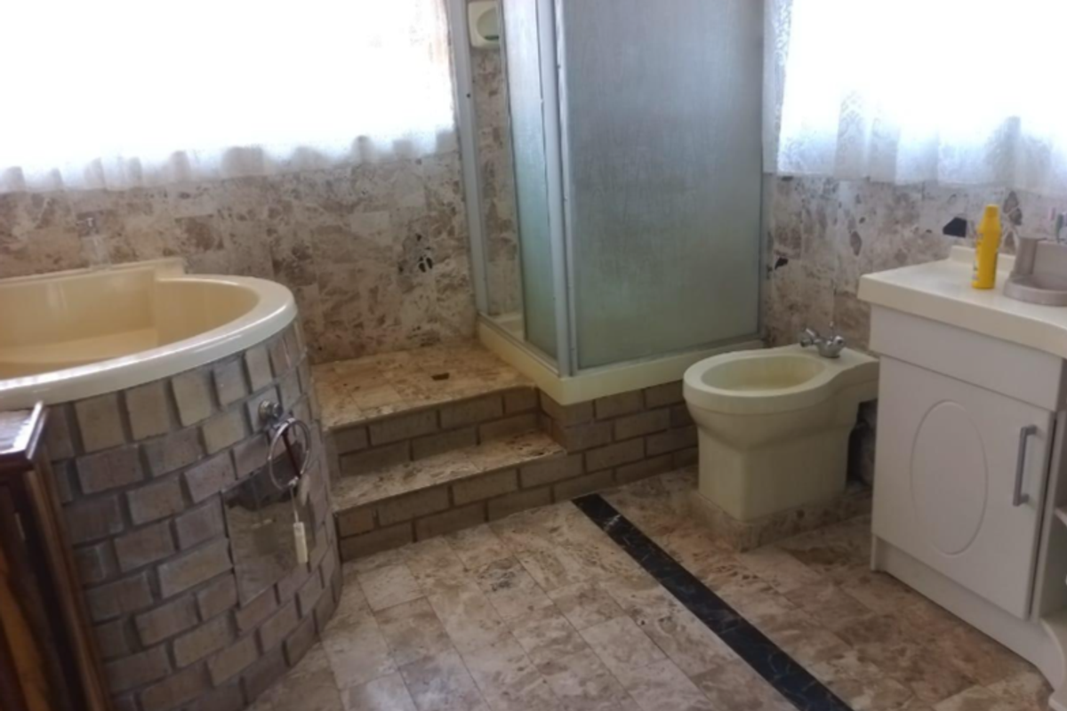 A dated bathroom featuring a built-in circular bathtub with brick cladding, a separate shower enclosure, a bidet, and a vanity unit with stone tiling.