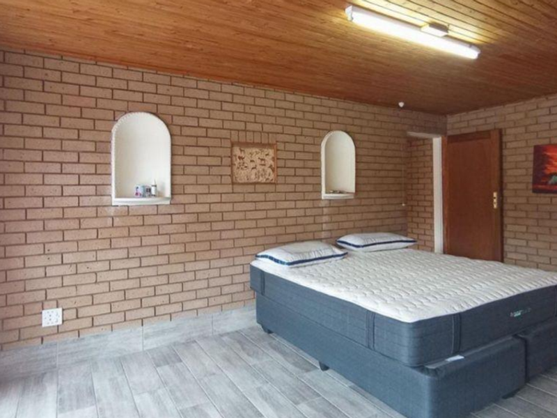 A bedroom featuring exposed brick walls, a timber ceiling, and tiled flooring, with built-in wall niches for storage.