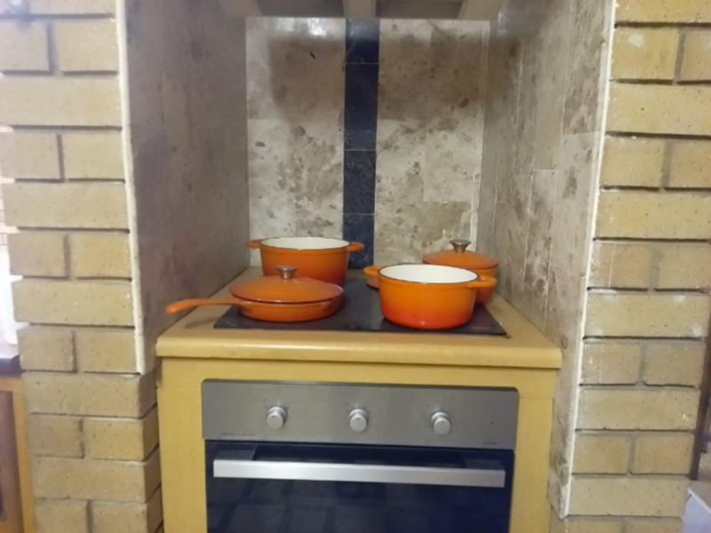 A kitchen cooking area featuring a built-in oven and electric cooktop set within a rustic brick masonry surround with stone tile backsplash.