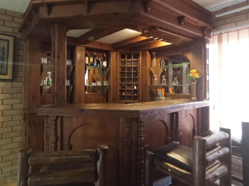 A dedicated home bar area featuring a custom-built wooden bar counter, integrated wine storage, mirrored shelving, and rustic exposed brick wall detailing.