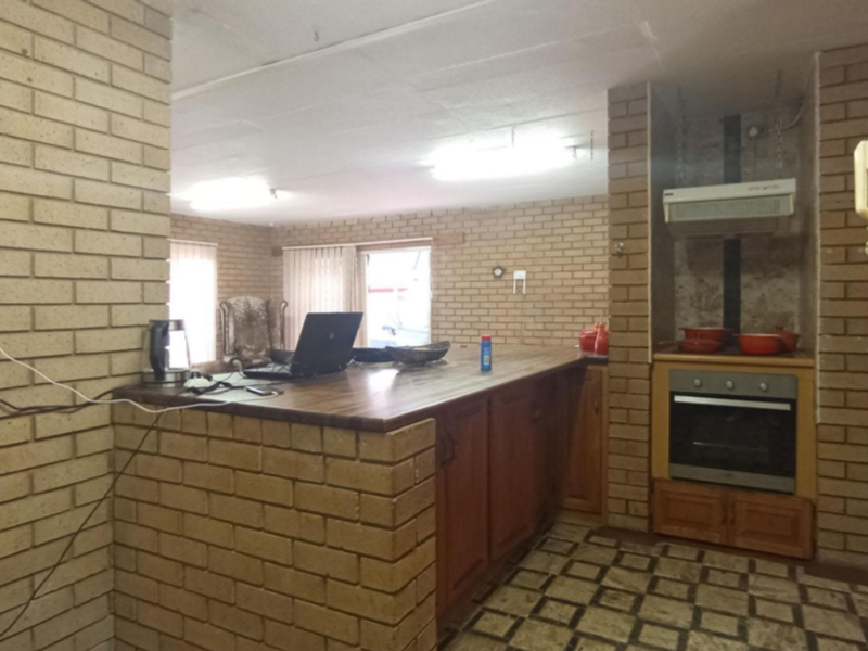 Open plan kitchen and living area featuring exposed brick walls, wooden cabinetry, and built-in oven with extractor fan.