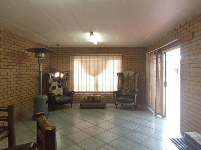 A covered patio area featuring exposed brick walls, tiled flooring, and a sliding glass door providing access to the outdoor space.