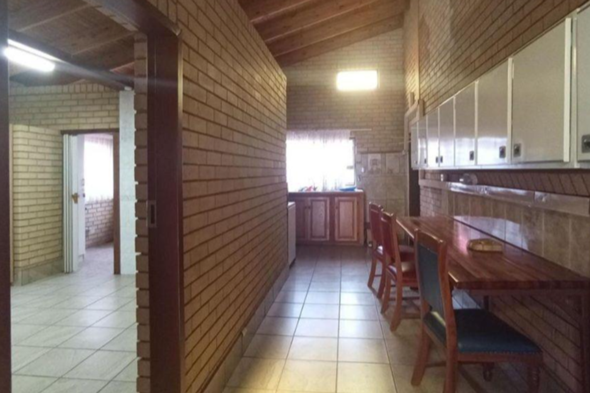A kitchen area featuring exposed brick walls, timber beam ceilings, tiled flooring, and built-in cabinetry with a wooden counter.
