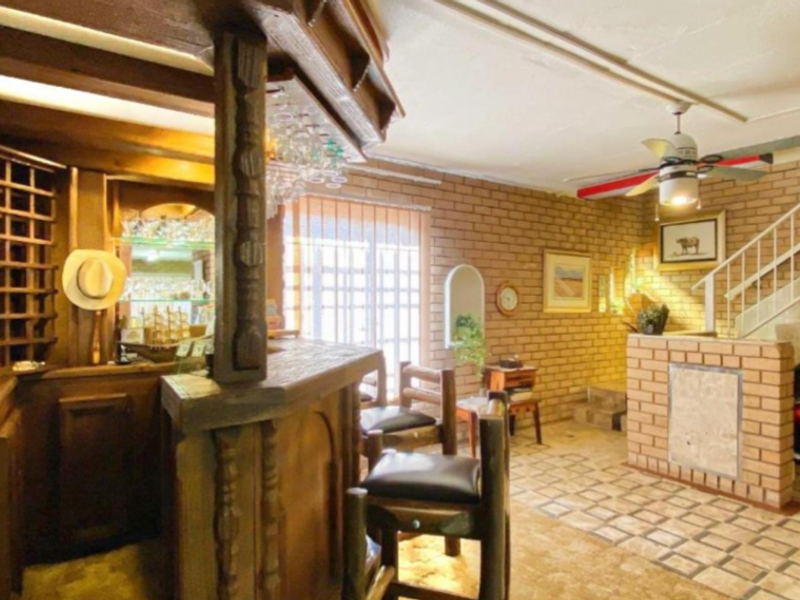 A rustic bar area featuring exposed brick walls, a built-in wooden bar counter, and an integrated staircase with a metal railing.