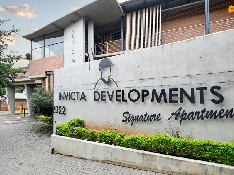Modern apartment complex entrance featuring a prominent concrete facade, professional signage, and paved driveway access.