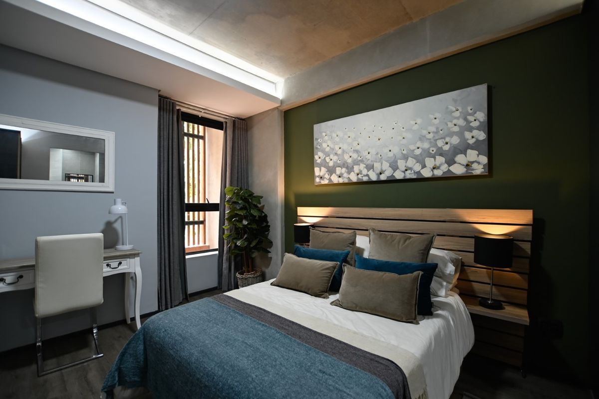 A modern bedroom featuring an exposed concrete ceiling, recessed lighting, and a custom built-in headboard with integrated bedside lighting.