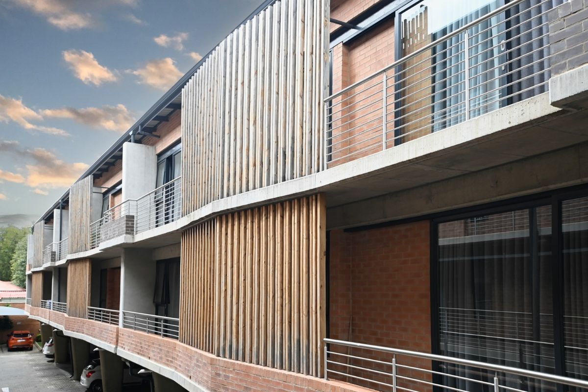 Modern apartment building exterior featuring exposed brickwork, concrete balconies with stainless steel railings, and decorative vertical timber slat privacy screens.