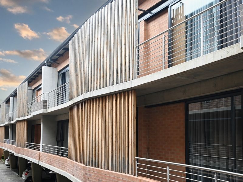 Modern apartment building exterior featuring exposed brickwork, concrete balconies with stainless steel railings, and decorative vertical timber slat privacy screens.