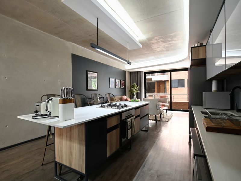 Modern open-plan kitchen and living area featuring a central island with gas hob, exposed concrete ceilings, and seamless access to a private balcony.