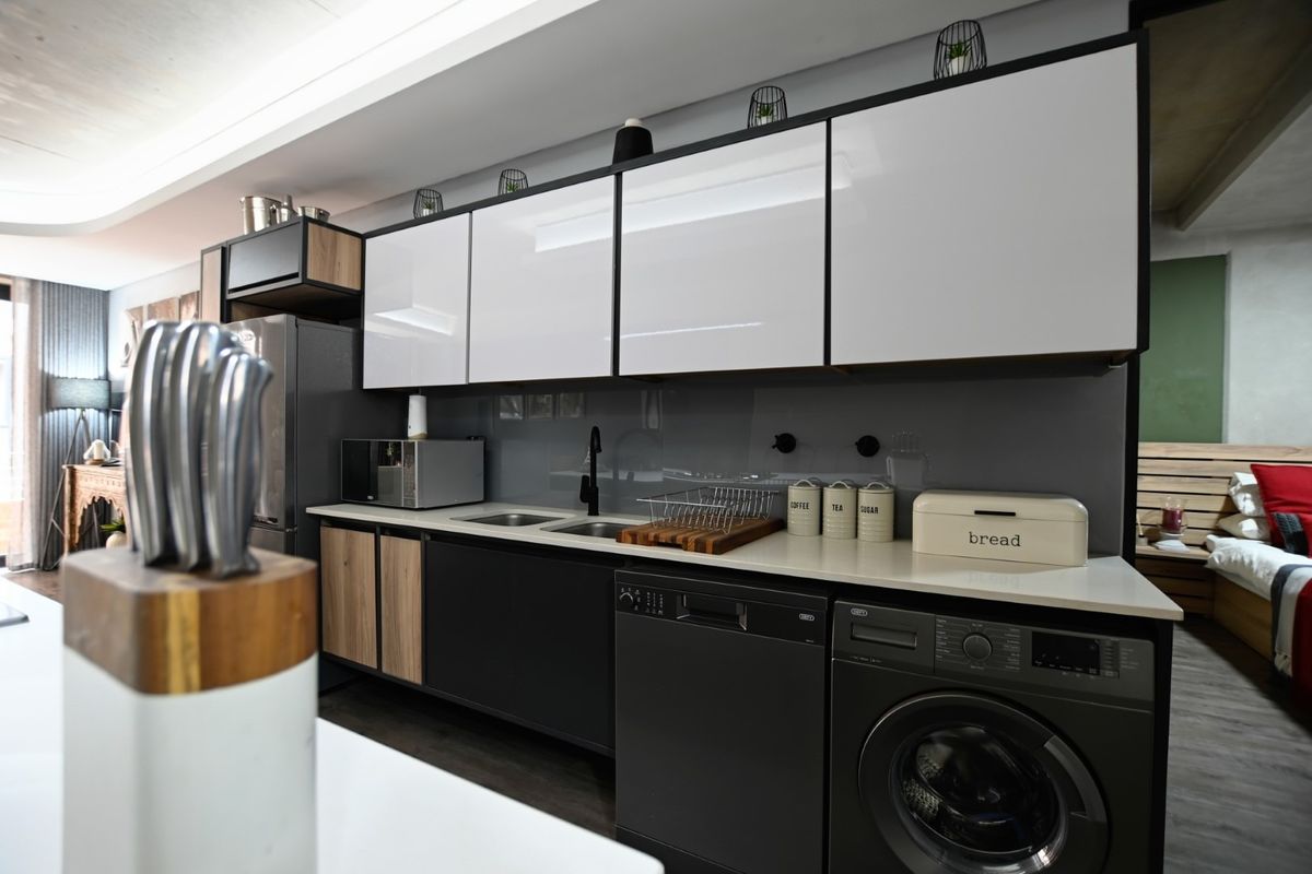 Modern kitchen featuring sleek two-tone cabinetry, stone countertops, integrated appliances, and a contemporary glass splashback in a well-maintained apartment setting.