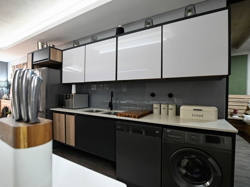 Modern kitchen featuring sleek two-tone cabinetry, stone countertops, integrated appliances, and a contemporary glass splashback in a well-maintained apartment setting.