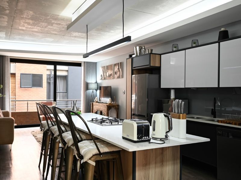 Modern open-plan kitchen and living area featuring a central island with gas hob, sleek cabinetry, and access to a private balcony.