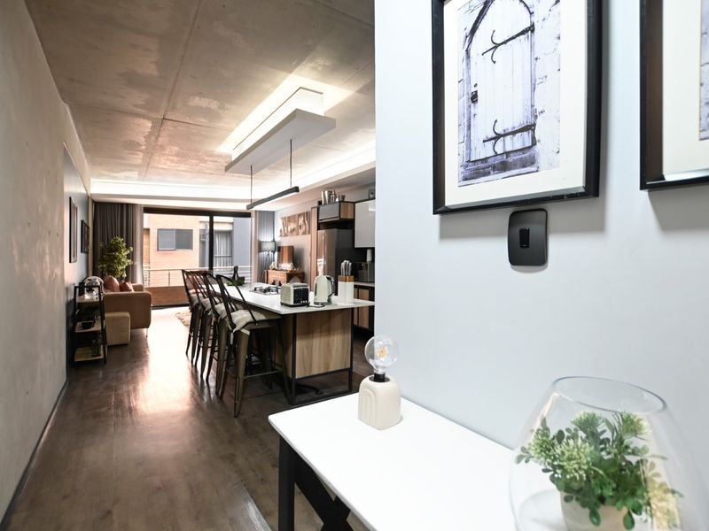 Modern open-plan living area featuring an exposed concrete ceiling, a central kitchen island, and seamless flow to an outdoor balcony space.