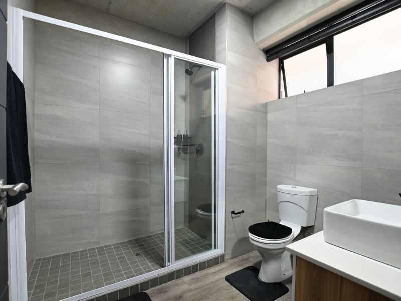 Modern bathroom featuring a walk-in shower with glass enclosure, vessel sink vanity, and neutral grey wall tiling.