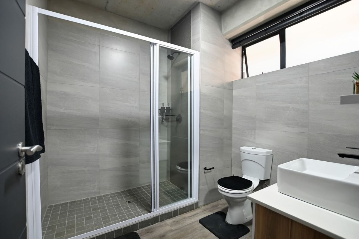 Modern bathroom featuring a walk-in shower with glass enclosure, vessel sink vanity, and neutral grey wall tiling.