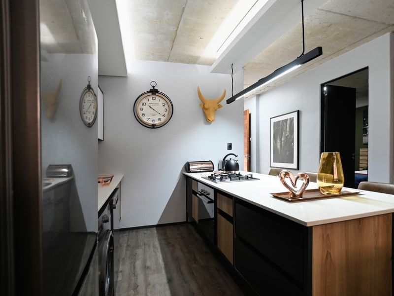 Modern kitchen featuring sleek cabinetry, stone countertops, gas hob, built-in oven, and stylish exposed concrete ceiling with contemporary linear lighting.