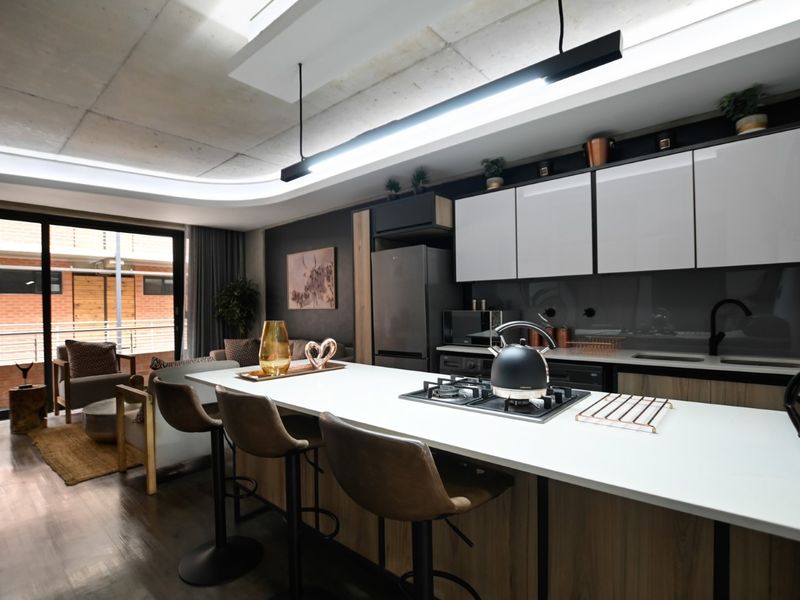 Modern open-plan apartment featuring a sleek kitchen with a central island, gas hob, and high-end finishes, seamlessly flowing into the living area.