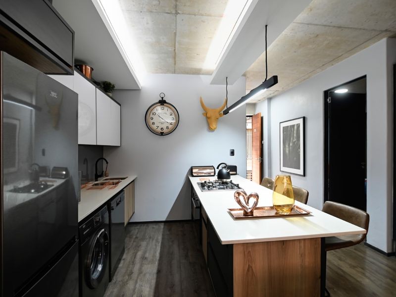 Modern kitchen featuring an island with integrated hob, sleek cabinetry, exposed concrete ceiling, and high-quality finishes in a contemporary open-plan layout.