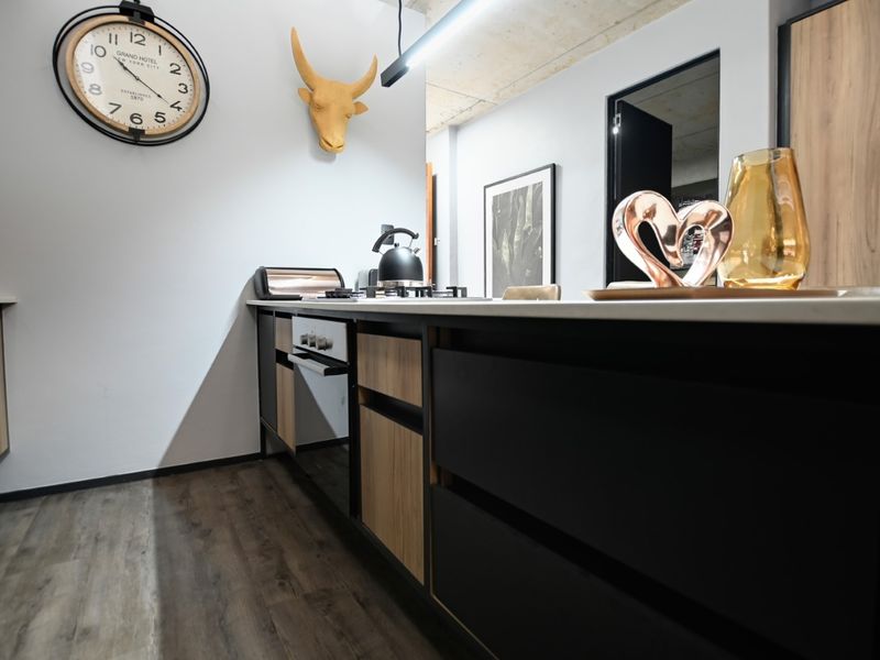 Modern kitchen featuring sleek two-tone cabinetry, stone countertops, integrated oven, gas hob, and stylish exposed concrete ceiling with contemporary lighting.