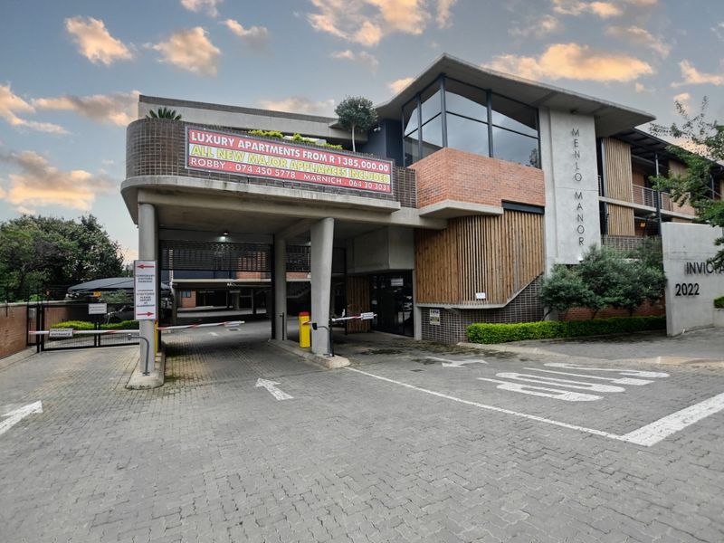 Front exterior view of Menlo Manor apartment complex featuring a paved driveway, secure boom gate access, and modern architectural facade with timber and brick detailing.
