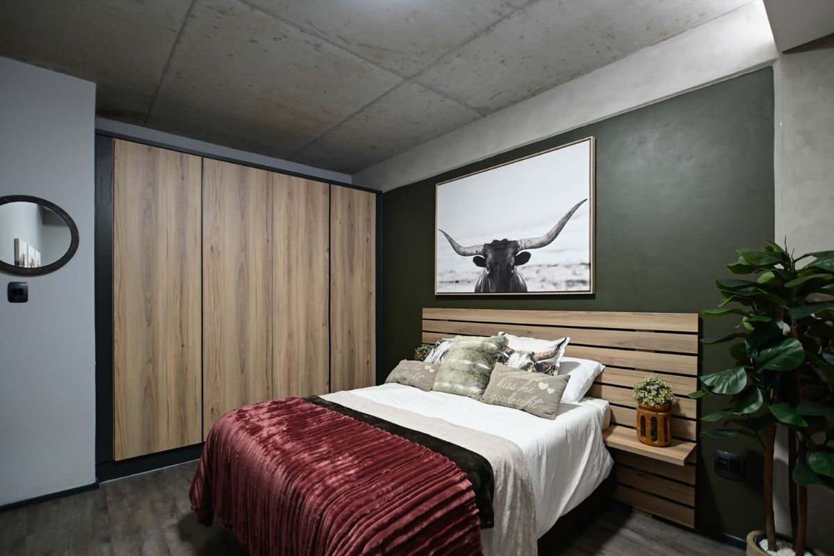 Modern bedroom featuring an exposed concrete ceiling, wood-finish built-in wardrobes, and a stylish dark green accent wall.